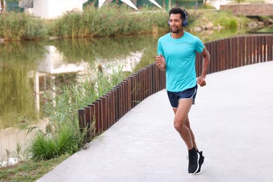 Photo of Smiling man in headphones running near river outdoors