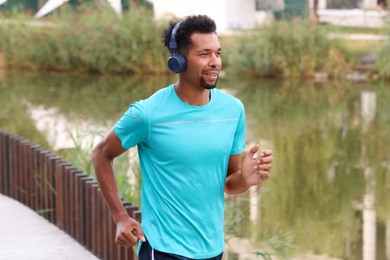 Photo of Smiling man in headphones running near river outdoors