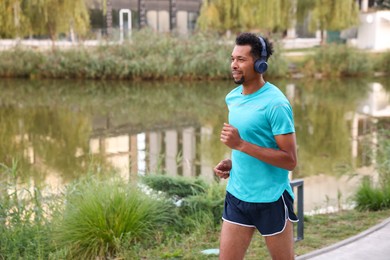 Photo of Smiling man in headphones running near river outdoors. Space for text