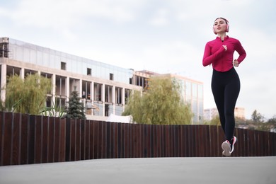 Photo of Beautiful woman in headphones running outdoors, low angle view. Space for text