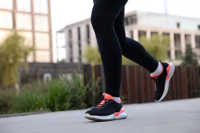 Photo of Woman in sneakers running outdoors, closeup. Space for text