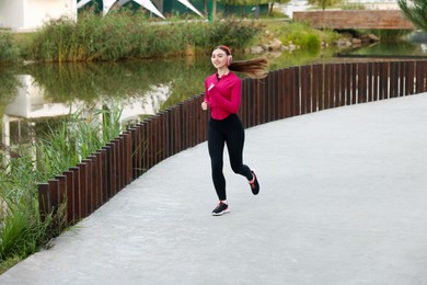 Photo of Smiling woman in headphones running near river outdoors
