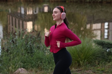 Photo of Smiling woman in headphones running near river outdoors