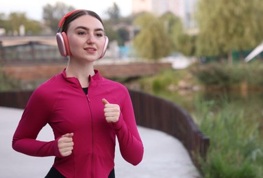 Photo of Smiling woman in headphones running outdoors. Space for text
