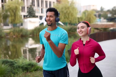 Photo of Smiling couple in headphones running near river outdoors