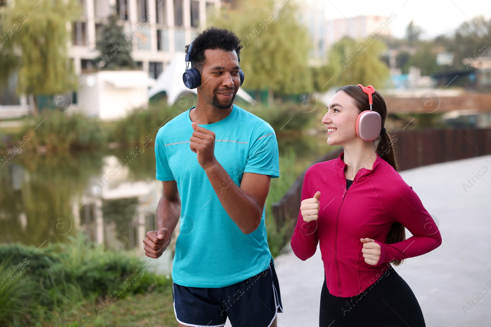 Smiling couple in headphones running near river outdoors Photo of Smiling couple in headphones running near river outdoors