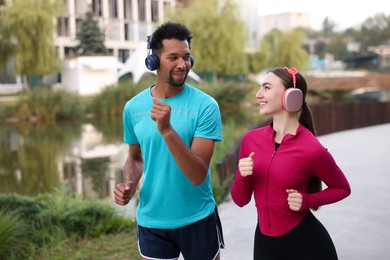 Photo of Smiling couple in headphones running near river outdoors