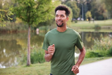 Photo of Smiling man running near river outdoors. Healthy lifestyle