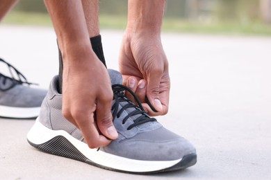 Photo of Runner tying shoelace of his sneaker outdoors, closeup. Space for text