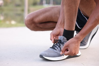 Photo of Runner tying shoelace of his sneaker outdoors, closeup. Space for text