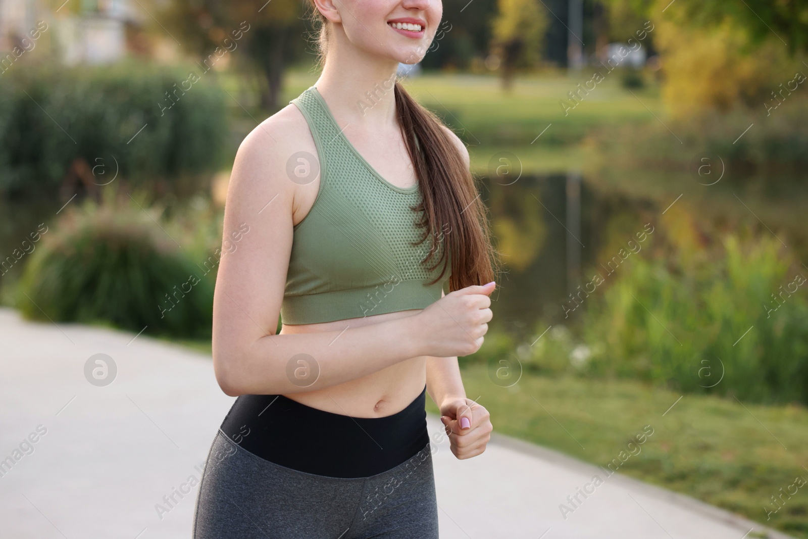 Photo of Smiling woman in sportswear running outdoors, closeup