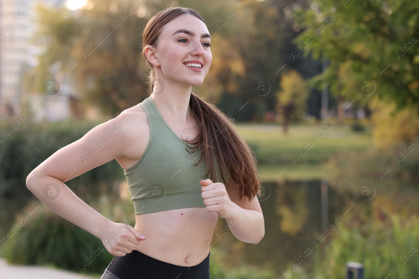 Photo of Smiling woman in sportswear running outdoors. Space for text