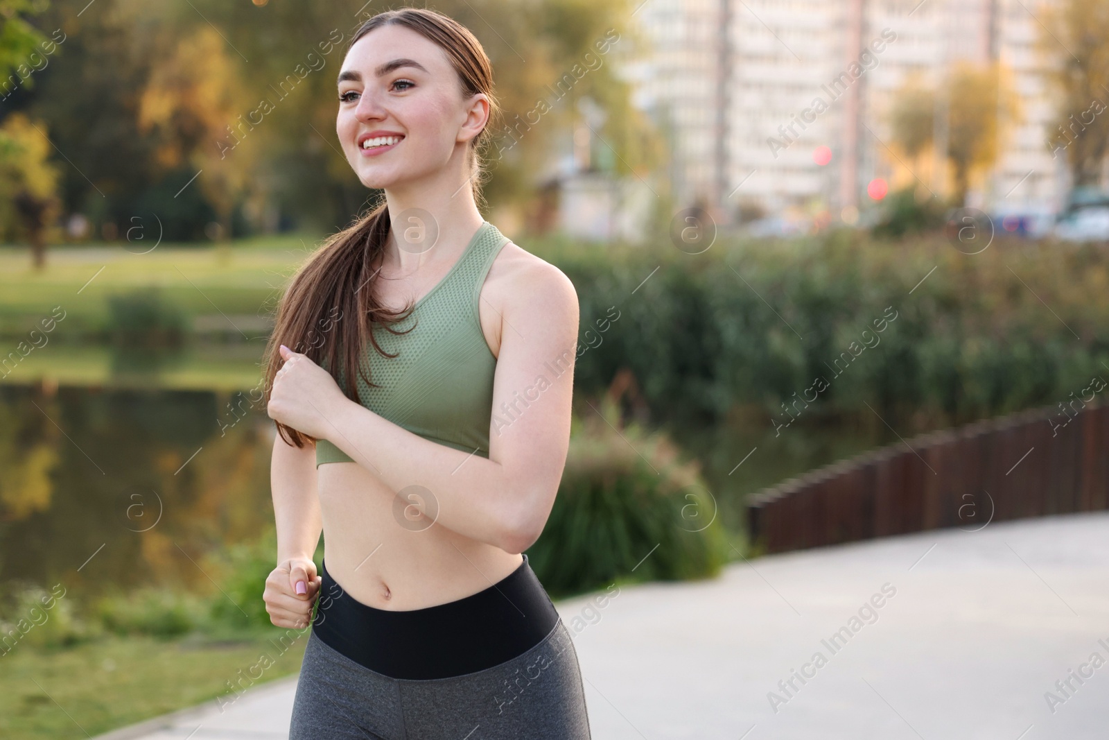 Photo of Smiling woman in sportswear running outdoors. Space for text