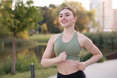 Photo of Smiling woman in sportswear running outdoors. Space for text