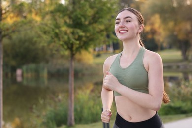 Photo of Smiling woman in sportswear running outdoors. Space for text