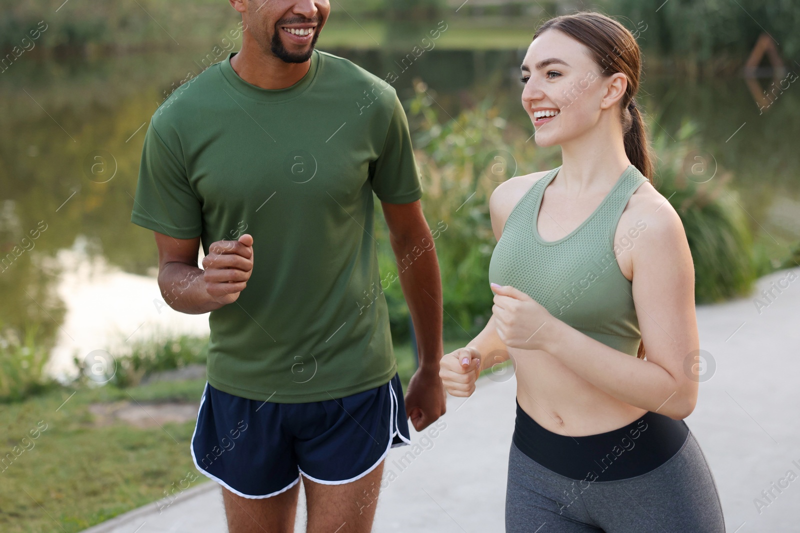 Smiling couple running near river outdoors, closeup. Healthy lifestyle Photo of Smiling couple running near river outdoors, closeup. Healthy lifestyle