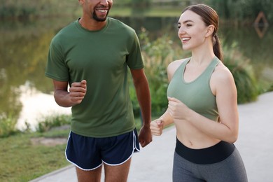Photo of Smiling couple running near river outdoors, closeup. Healthy lifestyle