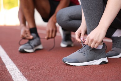 Photo of Runners tying shoelaces of their sneakers at stadium, closeup