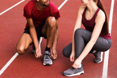 Photo of Smiling runners tying shoelaces of their sneakers at stadium, closeup