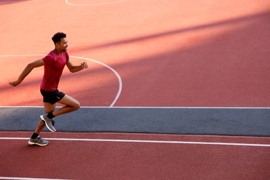 Photo of Smiling man in sportswear running at stadium. Space for text