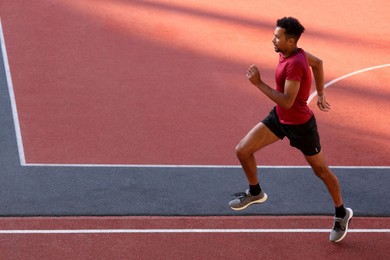 Photo of Handsome man in sportswear running at stadium. Space for text