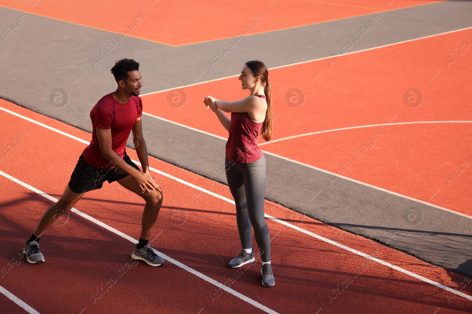 Photo of Smiling couple in sportswear doing warm-up exercises before run at stadium. Space for text