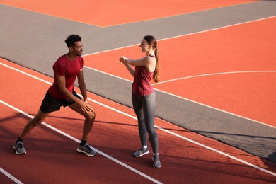 Photo of Smiling couple in sportswear doing warm-up exercises before run at stadium. Space for text