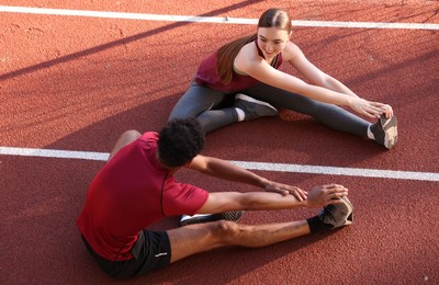 Photo of Couple in sportswear stretching before run at stadium, above view