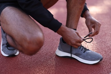 Photo of Runner tying shoelace of his sneaker at stadium, closeup