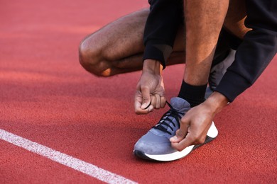 Photo of Runner tying shoelace of his sneaker at stadium, closeup. Space for text