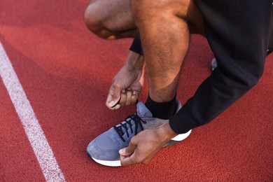 Photo of Runner tying shoelace of his sneaker at stadium, closeup