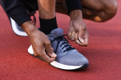 Photo of Runner tying shoelace of his sneaker at stadium, closeup