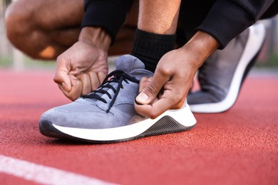 Photo of Runner tying shoelace of his sneaker at stadium, closeup