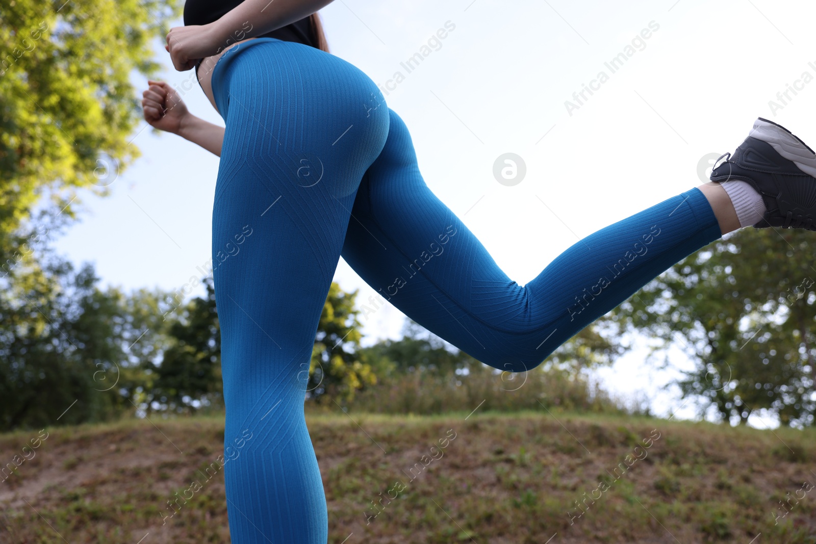 Woman in blue leggings running in park, closeup and low angle view Photo of Woman in blue leggings running in park, closeup and low angle view