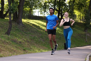 Photo of Smiling couple in sportswear running in park. Space for text