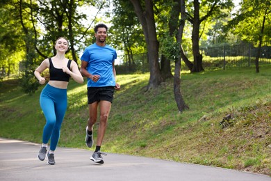 Photo of Smiling couple in sportswear running in park, low angle view. Space for text