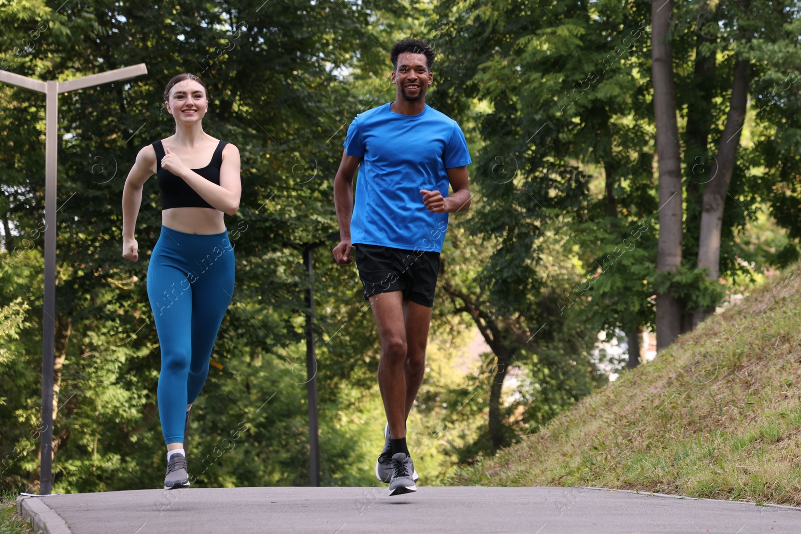 Photo of Smiling couple in sportswear running in park, low angle view. Space for text