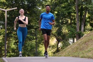 Photo of Smiling couple in sportswear running in park, low angle view. Space for text
