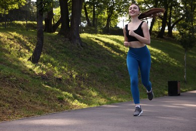 Photo of Smiling woman in sportswear running in park, low angle view. Space for text