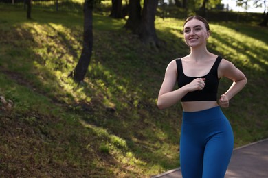 Photo of Smiling woman in sportswear running in park. Space for text