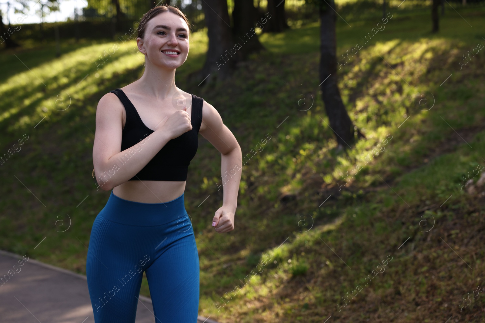 Photo of Smiling woman in sportswear running in park. Space for text