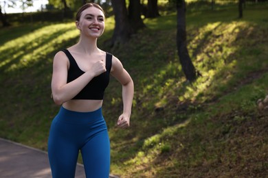 Photo of Smiling woman in sportswear running in park. Space for text