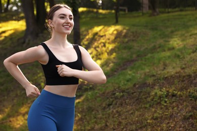 Photo of Smiling woman in sportswear running in park. Space for text