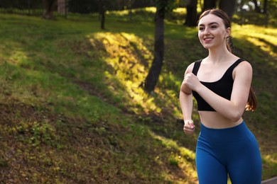 Photo of Smiling woman in sportswear running in park. Space for text