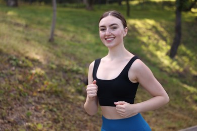 Photo of Smiling woman in sportswear running in park. Space for text