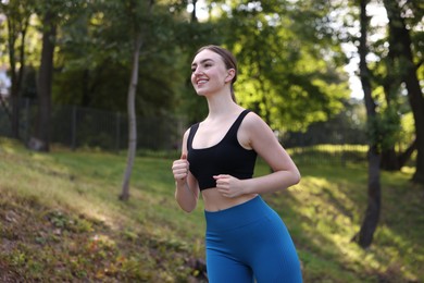 Photo of Smiling woman in sportswear running in park, low angle view