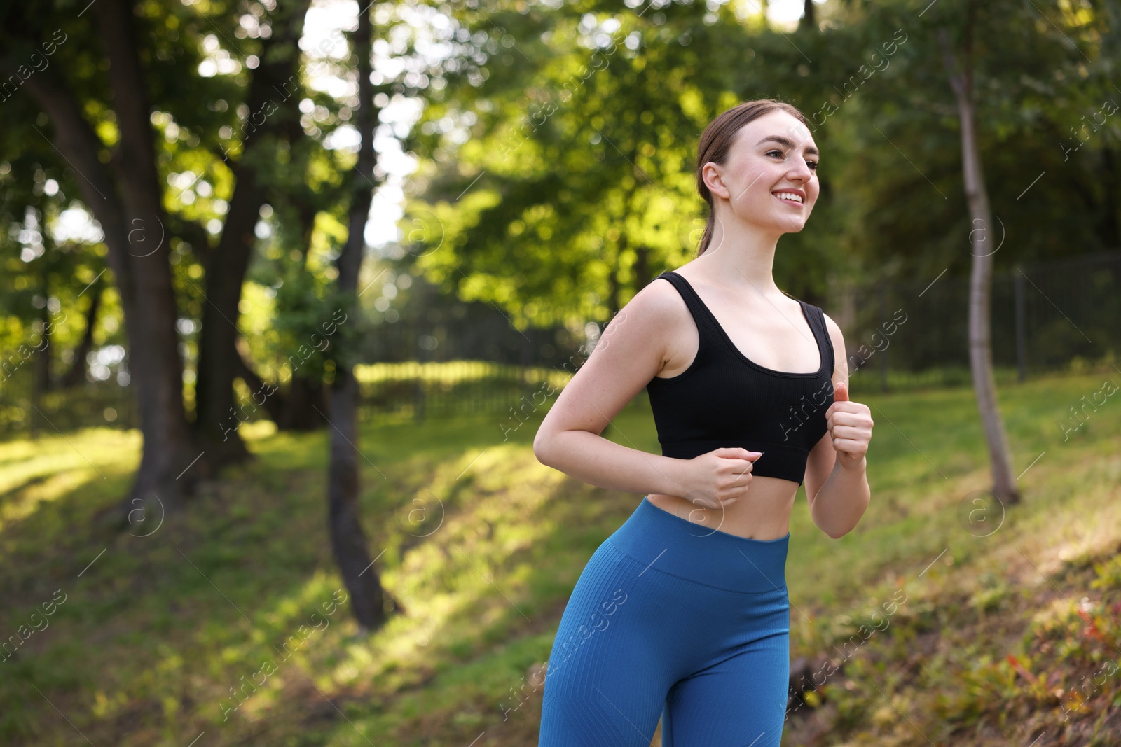 Photo of Smiling woman in sportswear running in park, low angle view. Space for text