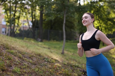 Photo of Smiling woman in sportswear running in park, low angle view. Space for text