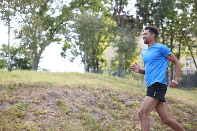 Photo of Smiling man in sportswear running in park, low angle view. Space for text