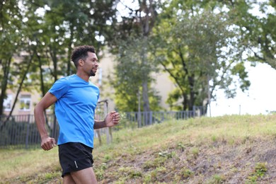 Photo of Handsome man in sportswear running in park, low angle view. Space for text